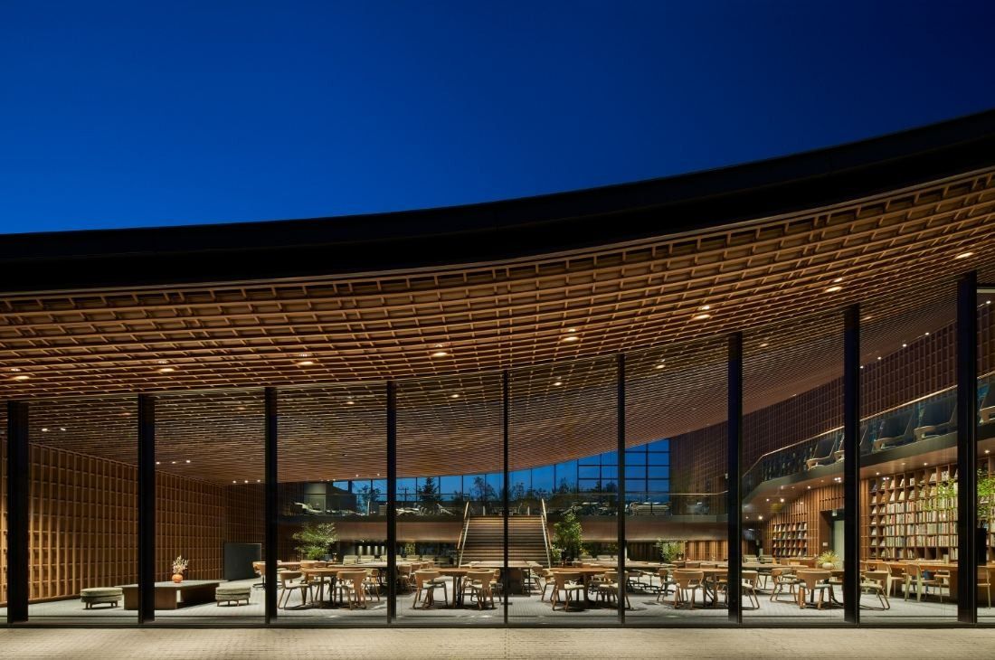ZOZO: Curved wooden lattice roof edge over a full-height glass wall, lit at dusk