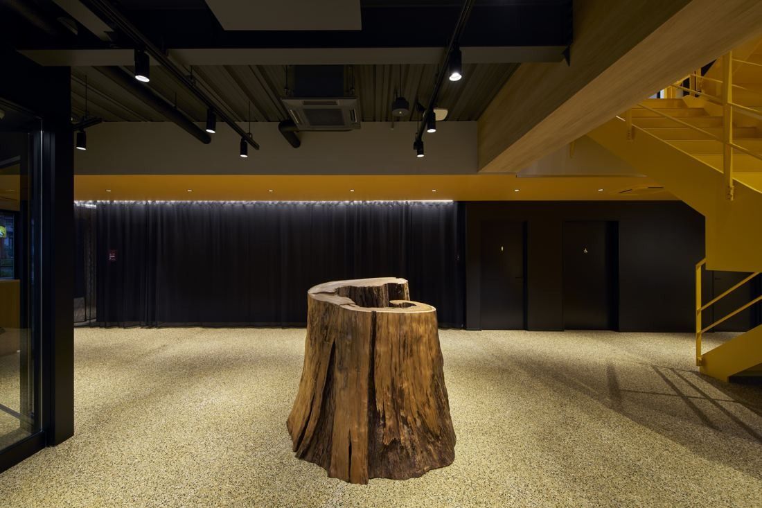 ZOZO: Dark entrance space with a tree stump on a gravel-like floor and a yellow stair