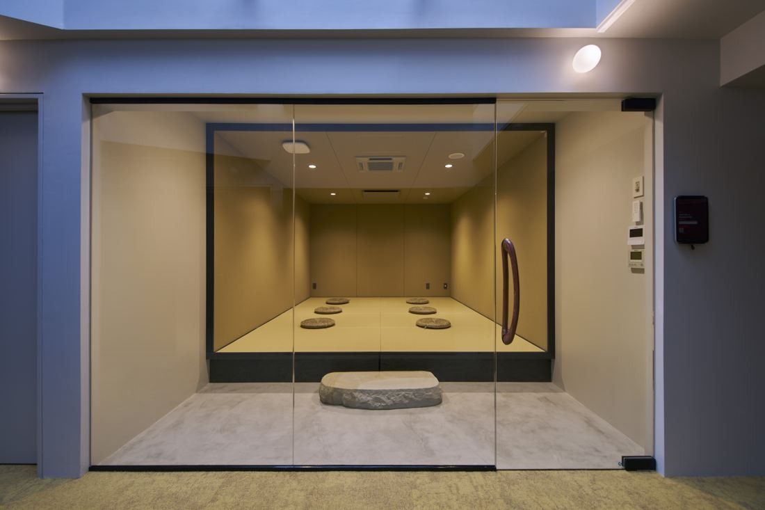 ZOZO: Glass-walled room with cushions on the floor and a flat stone in the centre