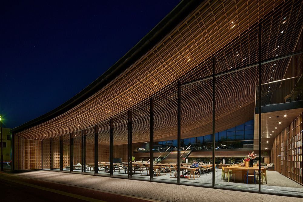 ZOZO: Lit glass facade under a timber lattice roof edge at night