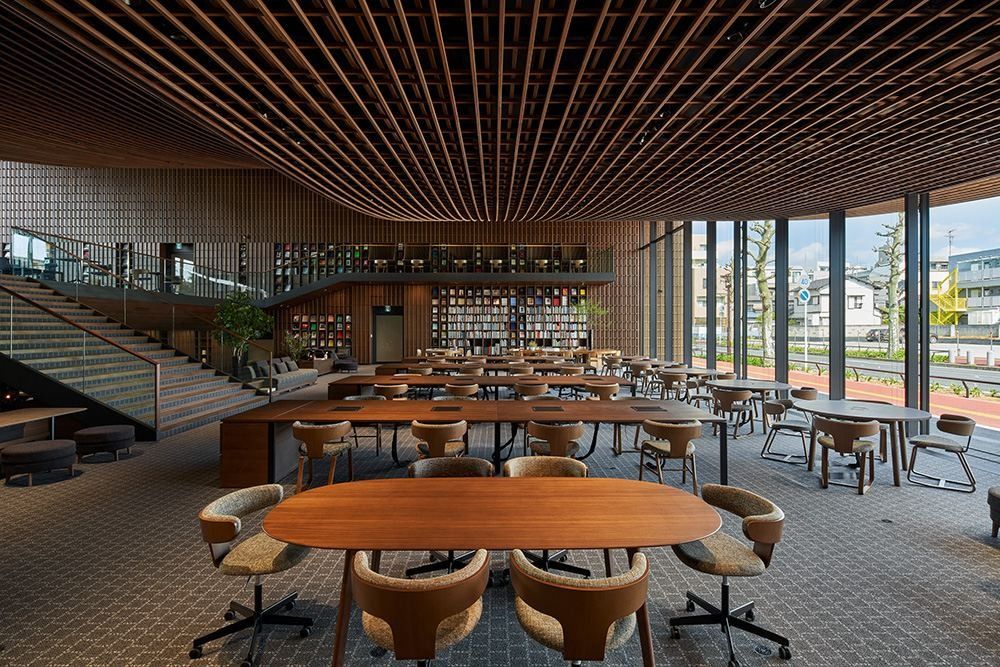 ZOZO: Oval wooden table with chairs, rows of desks and a bookshelf wall under a wooden ceiling