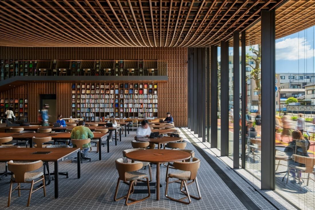 ZOZO: Round tables and a bookshelf wall beside full-height glass, with a few people working