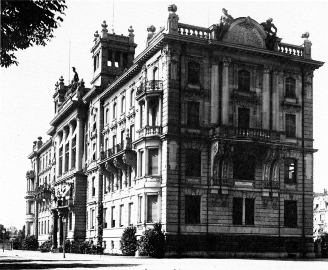 Black-and-white photo of a large ornate corner building with towers