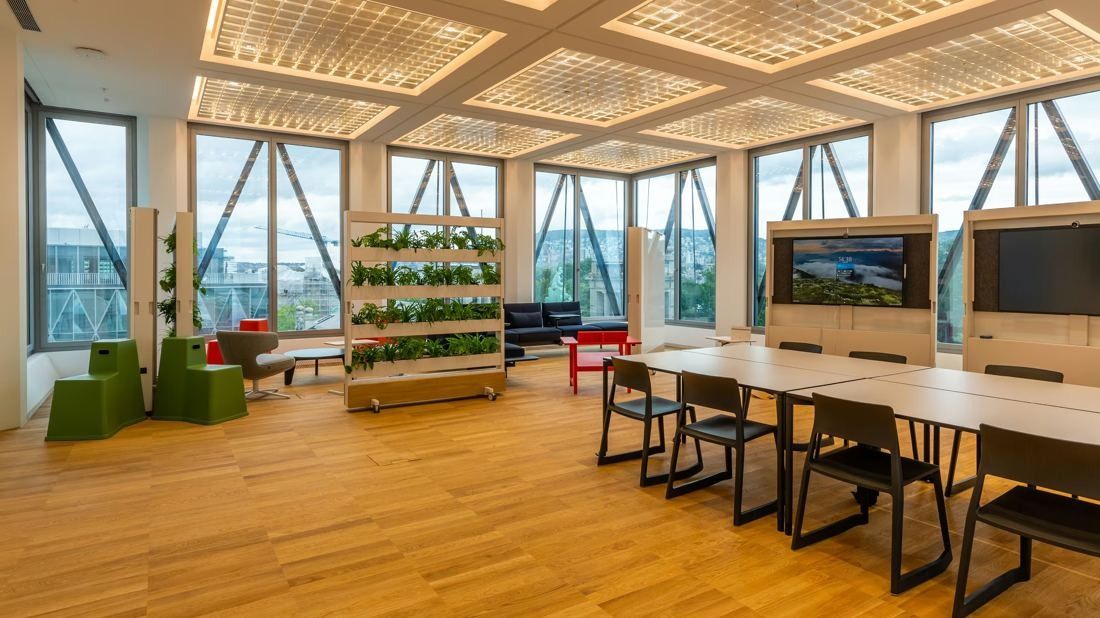 Zurich Insurance Group: Bright workspace with long tables, a plant shelf, screens and angled windows, oak floor