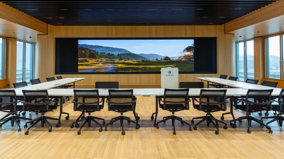 Zurich Insurance Group: Conference room with long tables, black chairs, wooden walls and a wide screen showing a landscape
