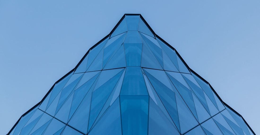 Zurich Insurance Group: Corner of a faceted blue glass facade rising to a point against a clear sky