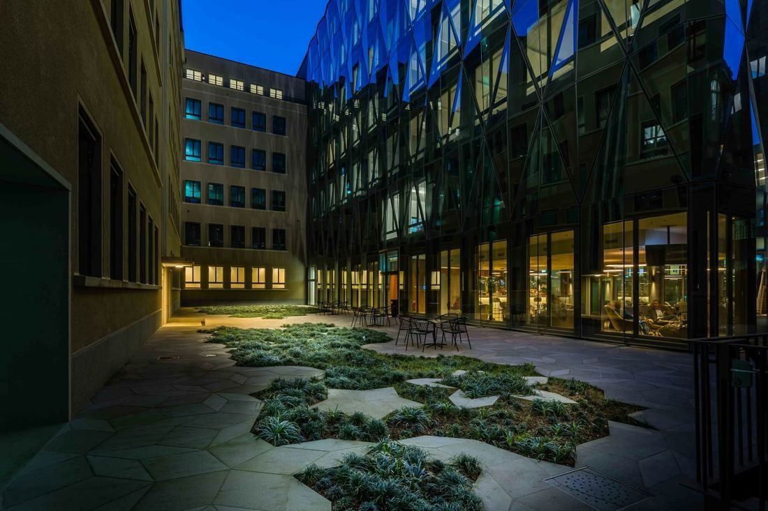 Zurich Insurance Group: Courtyard at dusk with low planting set into stone paving, lit windows and a glass facade around it