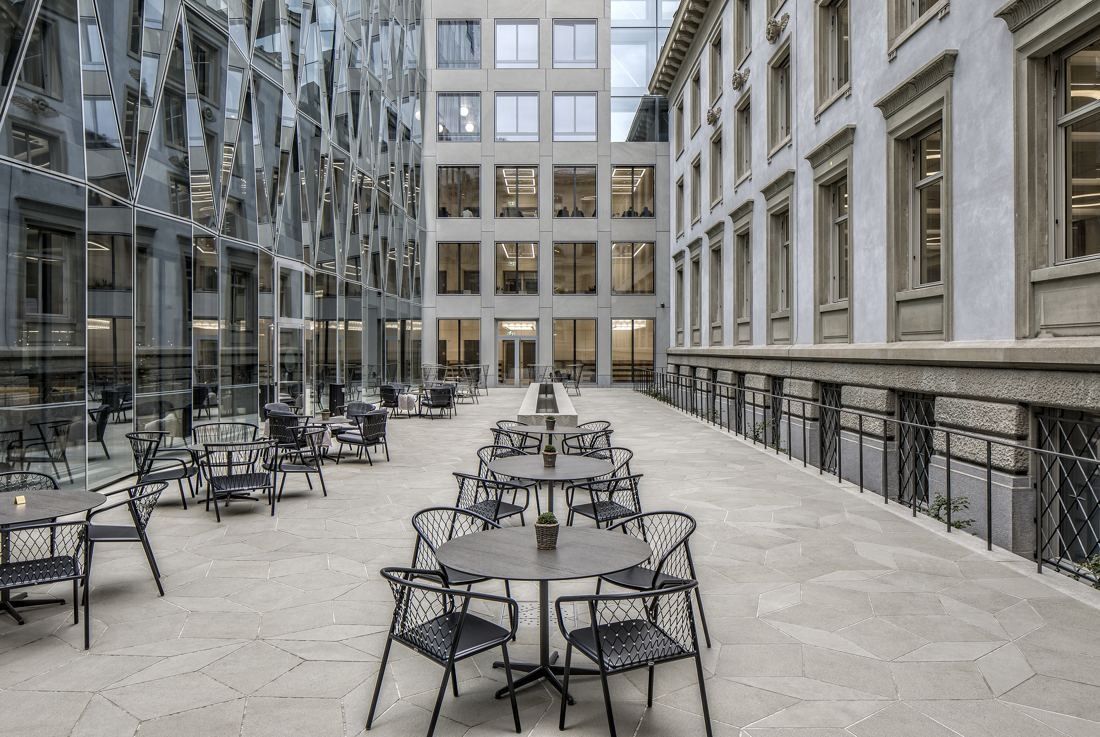 Zurich Insurance Group: Courtyard filled with round café tables and chairs between a glass facade and stone buildings