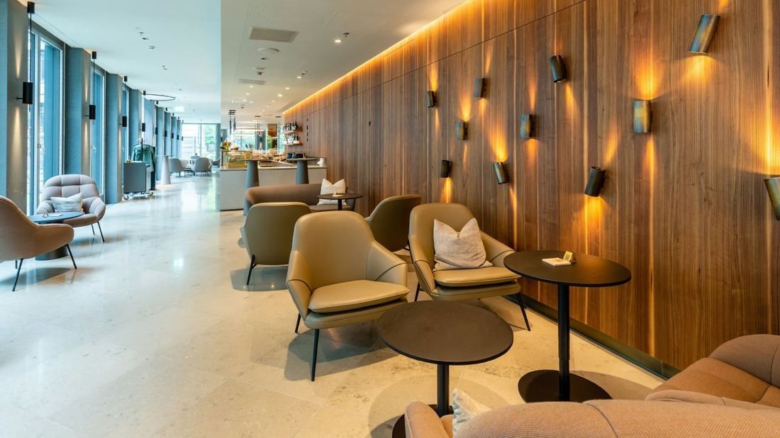 Zurich Insurance Group: Lounge with armchairs and small tables beside a wooden wall with wall lights