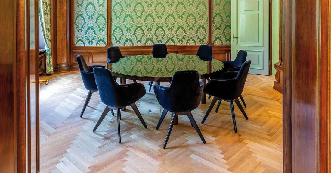 Zurich Insurance Group: Meeting room with a round table, dark chairs, herringbone parquet and green patterned wallpaper
