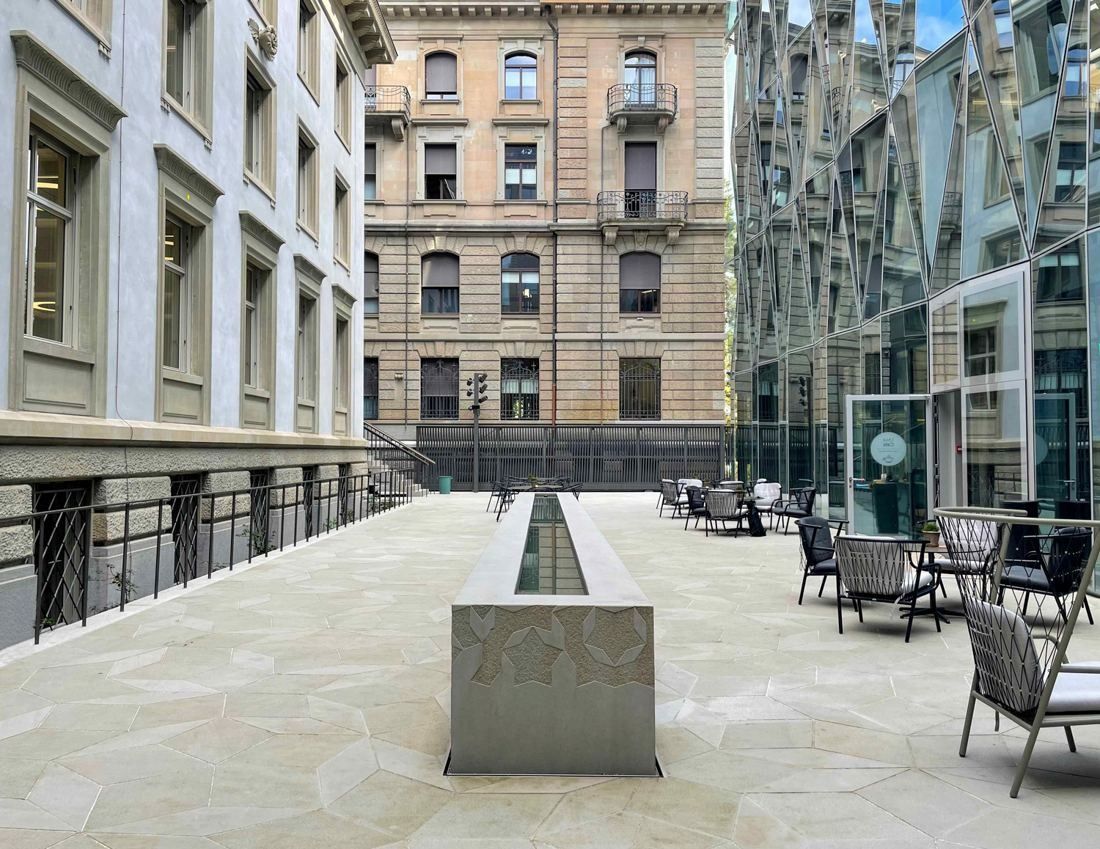 Zurich Insurance Group: Paved courtyard with a long stone fountain leading toward a historic facade, glass facade on the right