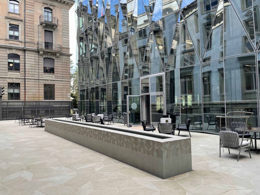 Zurich Insurance Group: Paved courtyard with a long stone trough, café tables, the historic facade on the left and the faceted glass facade on the right