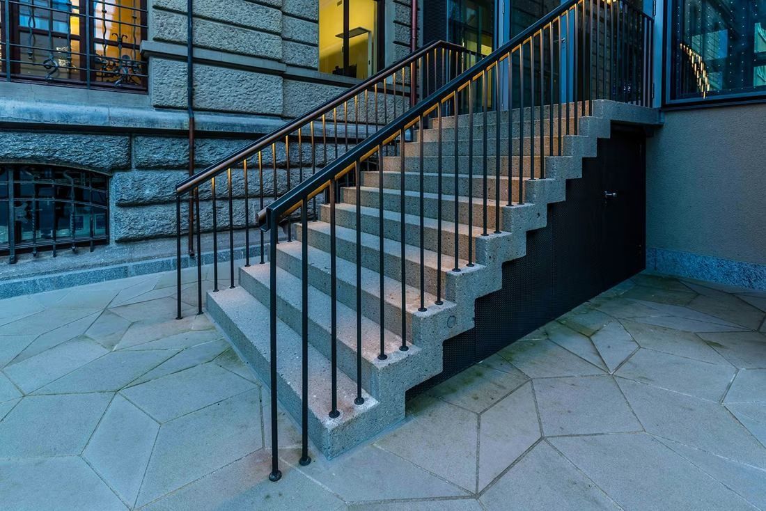 Zurich Insurance Group: Stone steps with black metal railings beside a rusticated stone wall, irregular paving below