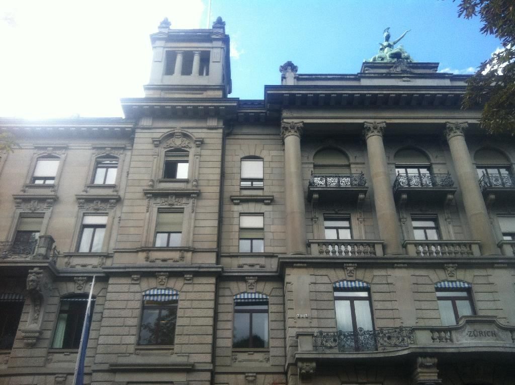 Zurich Insurance Group: Upper floors of an ornate stone facade with columns and a sculpture on the roof